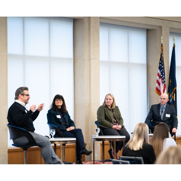 four people seated on stage in front of windows