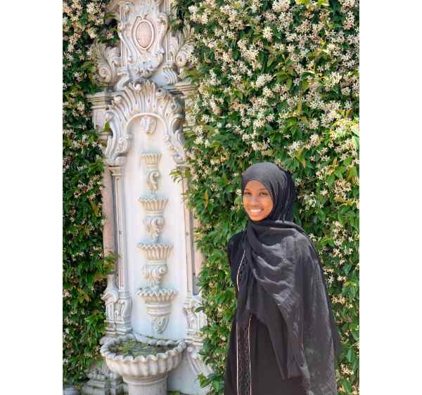 Yasmin Alemayehu stands by a sculpture next to a wall of greenery