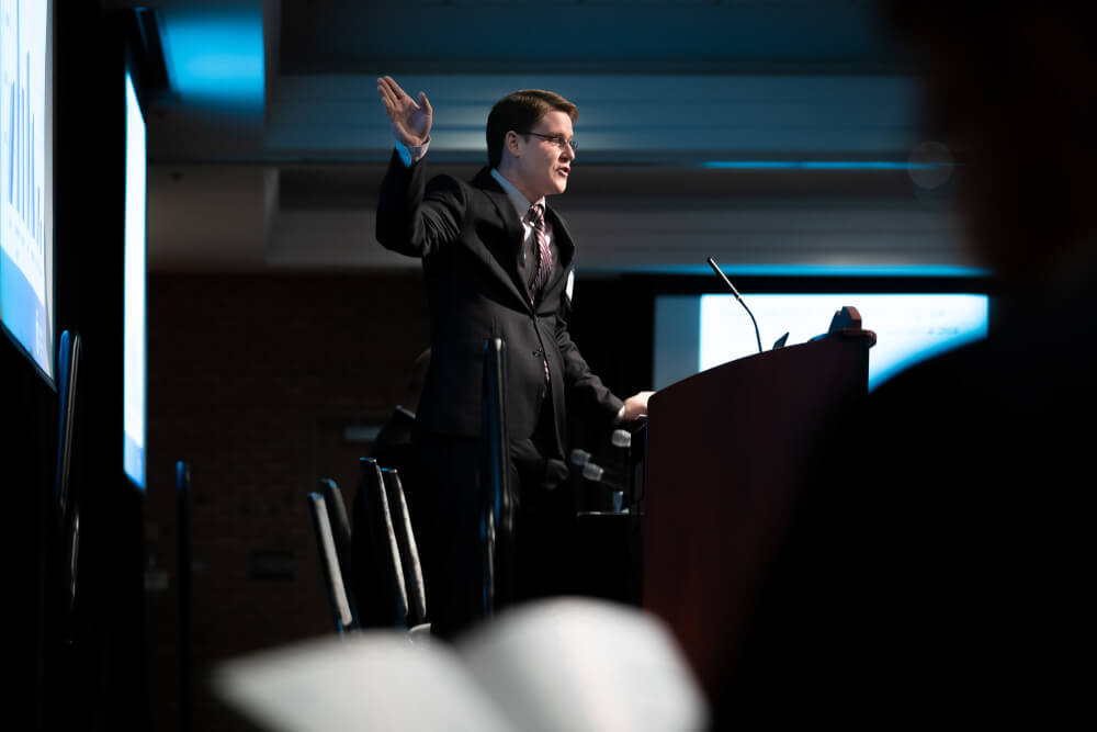 man at podium pointing to screen