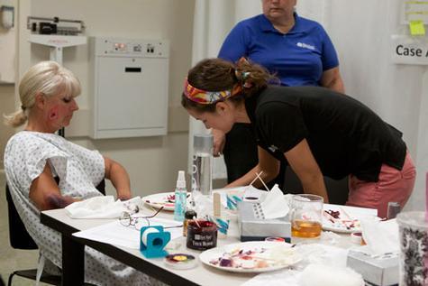 Lab supervisor Ashley West applies makeup to Laurie Elders, one of the standard patients participating in a burn simulation.