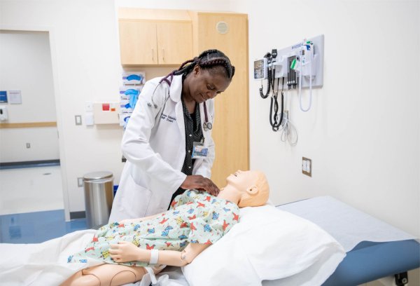 nursing student in white lab coat works on a manikin