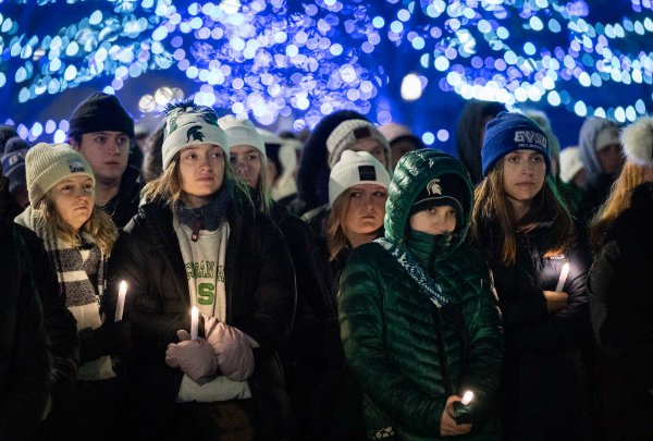 Students stand outside at the vigil. Some wear MSU hats, and some wear GVSU hats. 