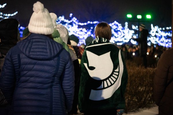 Two girls stand at the vigil. One is wearing a blue coat and white hat; the other is wrapped in a blanket with an MSU logo.