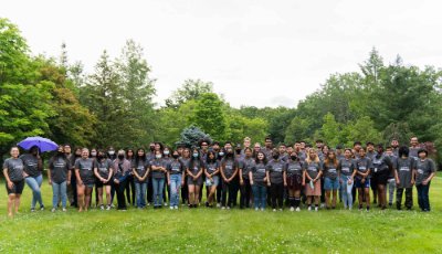 large group of high school students in TRIO Upward Bound t-shirts standing in two rows outside against a background of trees
