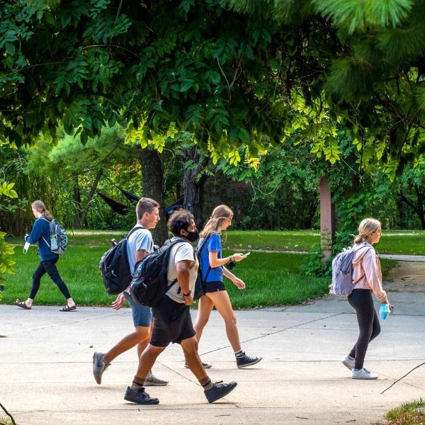 people walking on campus on sidewalks, green trees and green grass