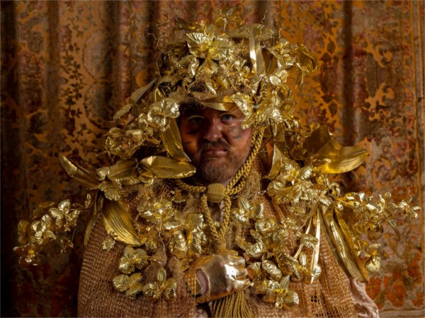 A person with a beard wears elaborate gold headwear.