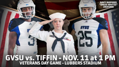 Two GVSU football players holding American flags with a uniformed military officer saluting