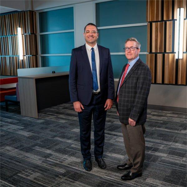 Two people stand in a posed photo. They are standing in the DeVos Center for Interprofessional Health.