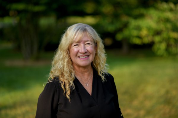 A person standing with greenery in the background smiles for the camera.