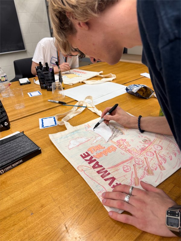 A person uses a marker on a drawing that includes the words "the voyage" and #vmake