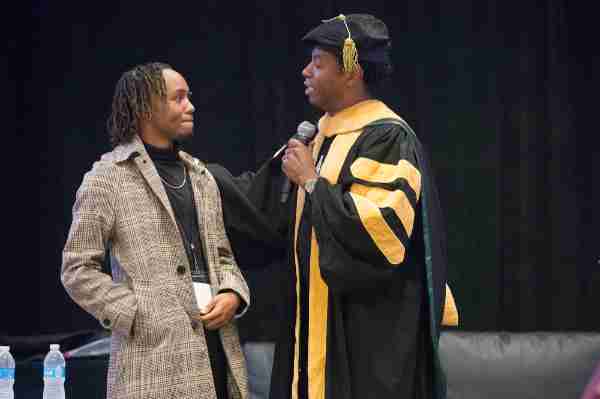 Adolph Brown, right, in academic regalia, speaks to a conference attendee on stage