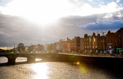 Buildings in Dublin seen along a waterfront. A beam of sun shines on the river.