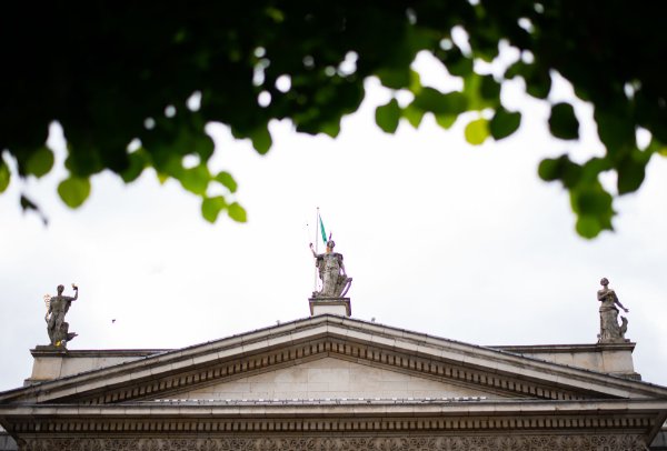 The top of a building with three statues with the Irish flag flying behind the middle statue