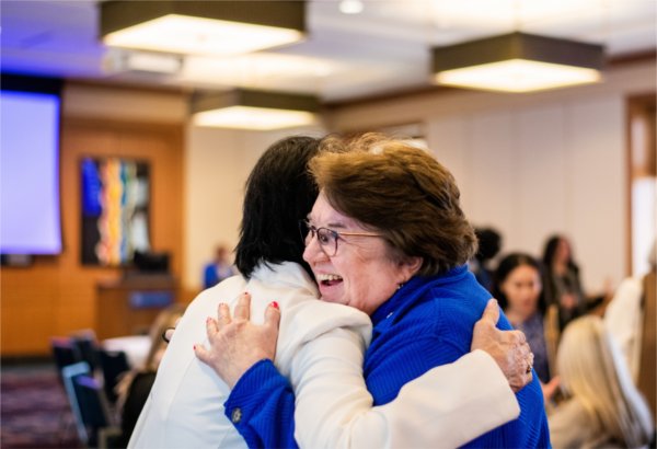 A university president and a faculty member hug. 