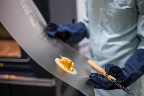 hands in gloves holding a thin metal sheet with a 3D object on it