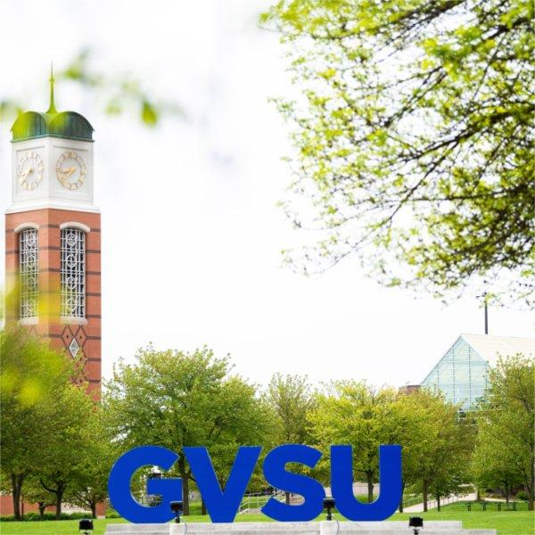 The blue GVSU letters are in the foreground on the Valley Campus and the Cook Carillon Tower is in the background.