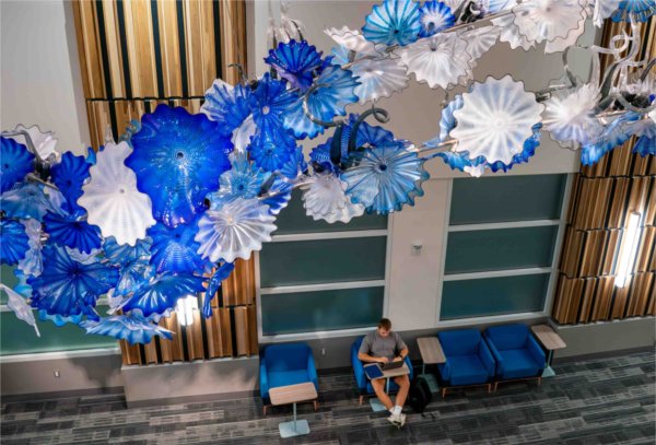 A student studies beneath an art glass sculpture in an academic building. 