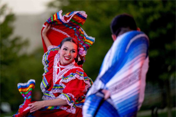  Two dancers wearing traditional colorful Hispanic folk clothing dance on a stage. 