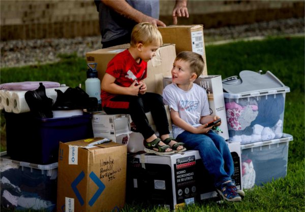  Two young children sit on boxes of belongings being moved into a college dormitory. 