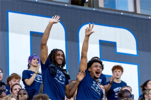 College students raise their hands in the air with big smiles on their faces.  