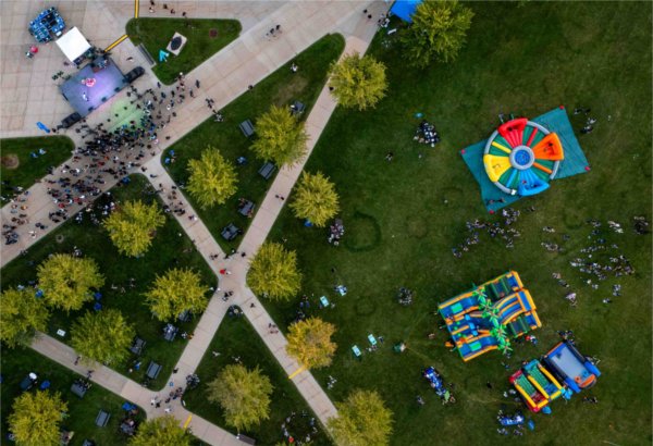 As seen from a drone, colorful carnival games are seen as people mingle during a welcome event. 