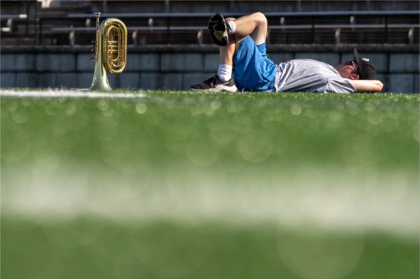  A band member with their instrument rests on a football field. 