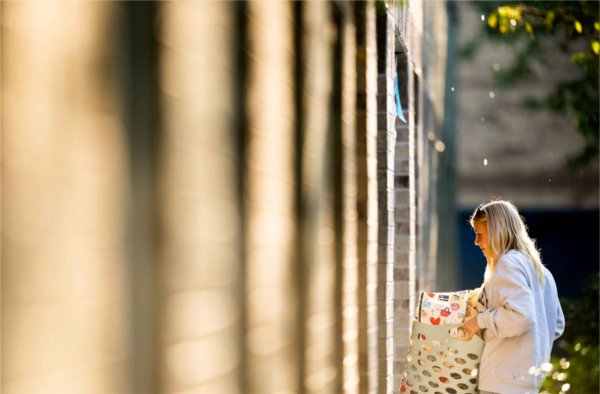  Golden light hits the side of a housing unit as a student carries in a basket of belongings. 