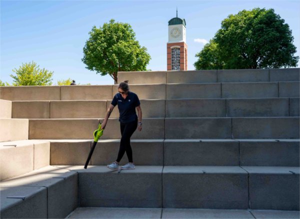  A person blows leaves off of an amphitheater area with a carillon tower in the background. 