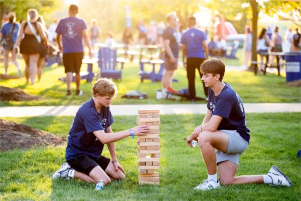  Two college students kneel in the grass as they play Jenga, a wooden game. 