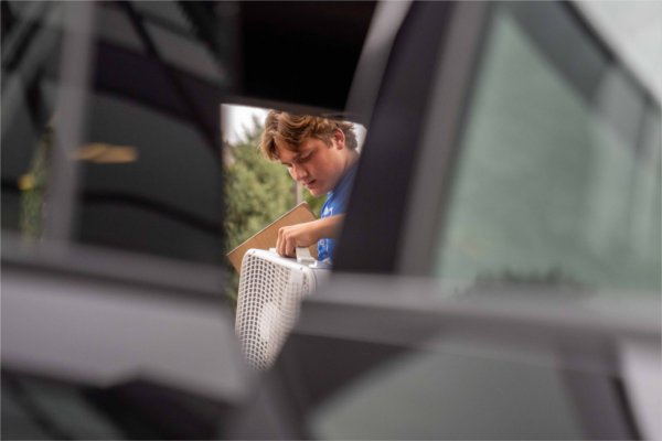  A college student seen through an opening in a car door hauls a fan during move-in. 