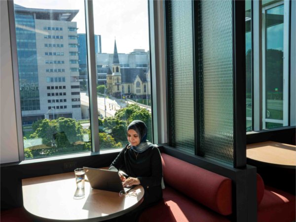  A person works on a laptop computer near a window with a cityscape behind them. 
