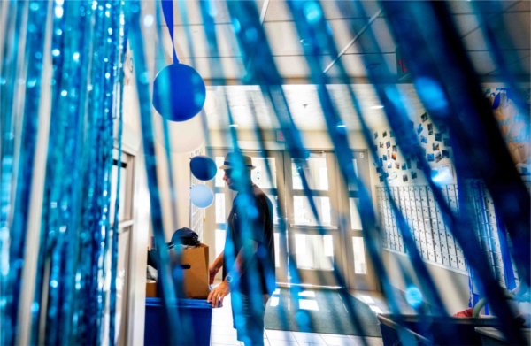  A person wearing a hat is seen through blue streamers as they push a cart of belongings into a housing unit. 