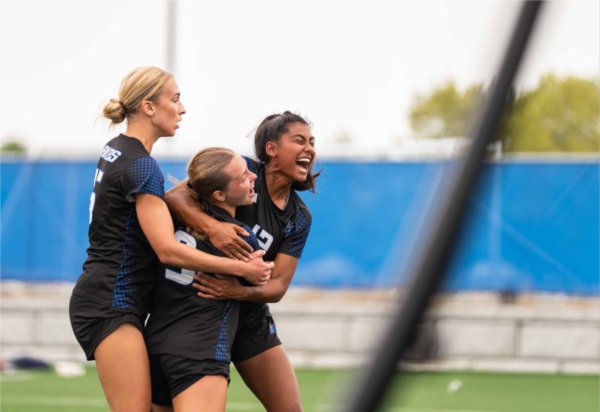  College women's soccer players react to a goal. 