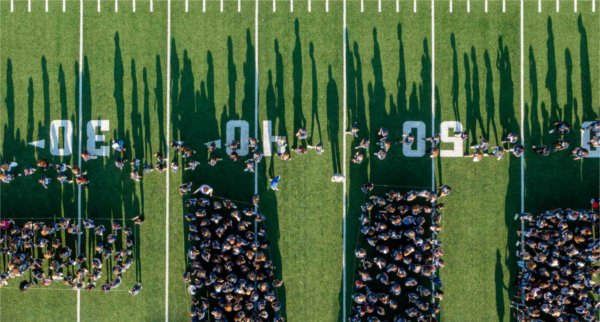  As seen from a drone, students cast long shadows on a football field. 