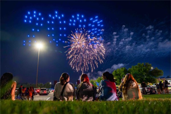  College students sit in the grass to watch colorful fireworks. 