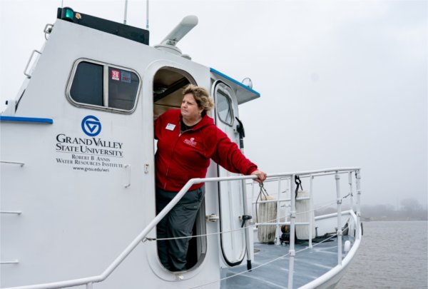 A boat captain wearing red hangs out of the door of the boat. 