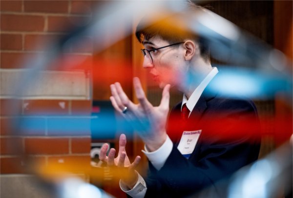  A college student gestures with his hands as he talks about his research as seen through a sculpture.
