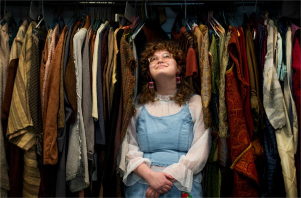  A college student poses for a portrait as they pose among theatre costumes. 