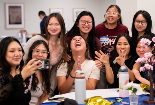  A group of smiling and laughing college students as they take a group selfie during an event. 