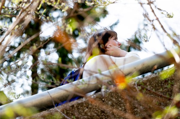 A college student is seen through greenery as they listen to a tour.  