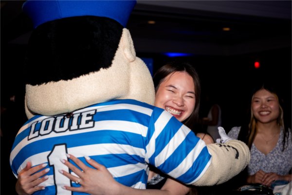 A college student smiles as they hug a college mascot, Louie the Laker. 