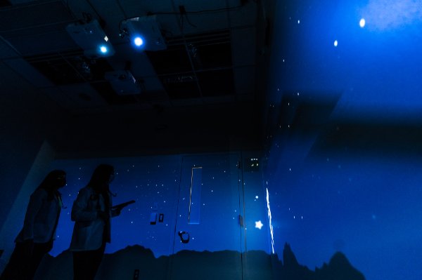 Two silhouetted bodies stand in a room with glowing blue walls covered in stars.