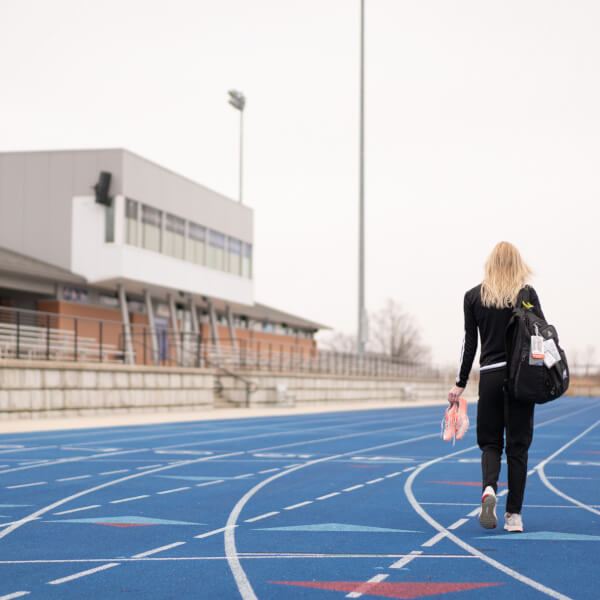 woman holding track spikes walking on empty track