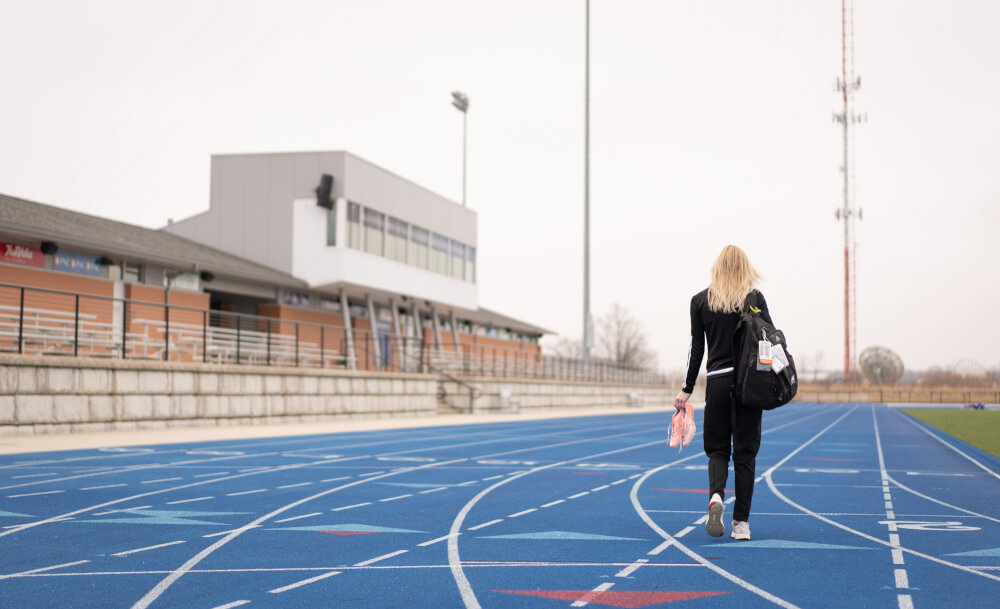 woman holding track spikes walking on empty track