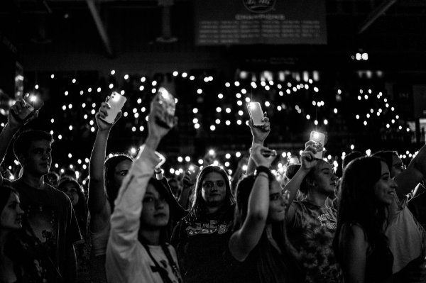 Students use cell phones to shine lights in an arena. Lights are seen all around.
