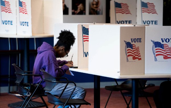 A person is seated while voting. A partition has an American flag and the word "vote."
