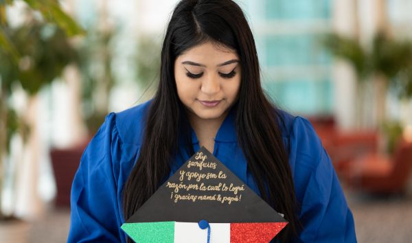 A person holds a graduation cap with writing and the colors green, white and red on it.
