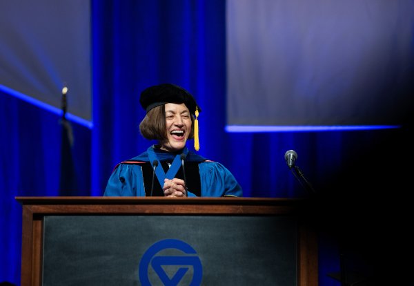 A person wearing academic garb smiles while standing at a podium.
