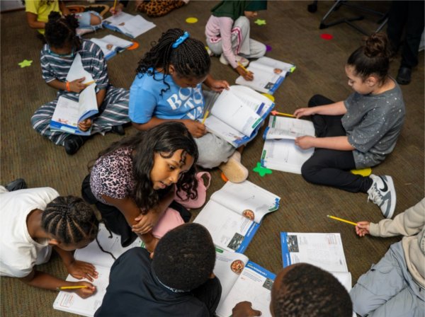 Third graders sit on the floor with open math workbooks