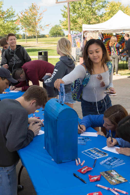 Student smiling while putting postcard in mailbox